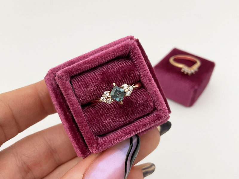 Hand holding a Rose gold Alexandrite gemstone and diamond ring in pink box