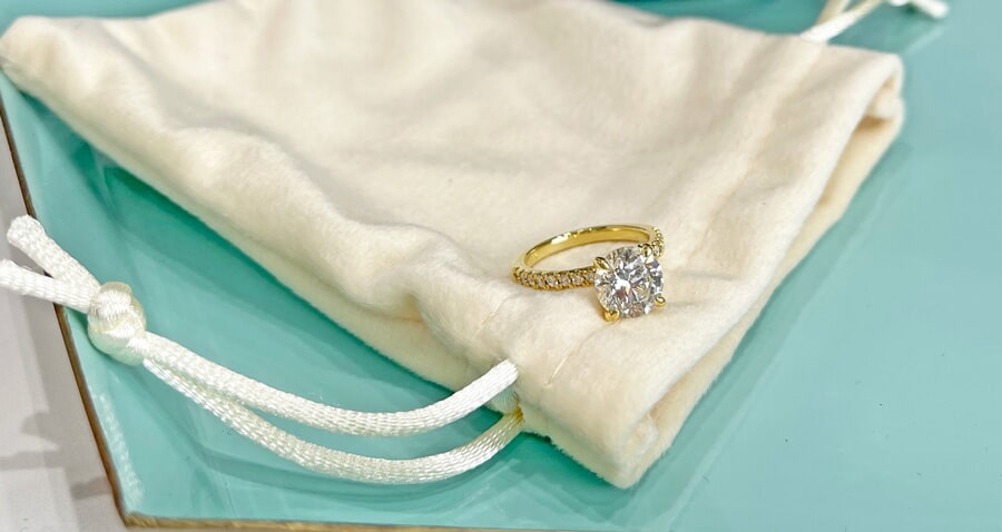 Round diamond ring with yellow gold diamond band on a soft light blue pouch.